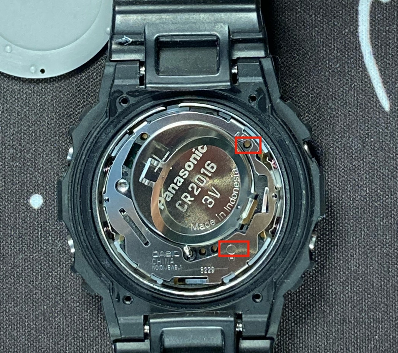 Casio G-Shock DW-5600: Cómo resetear el reloj mediante el contacto AC: colocas una punta de la pinza en el círculo que hay debajo del (-) en la foto y la otra punta en el agujero señalado por la flecha de la placa metálica donde pone AC. Haces contacto durante unos 3 segundos. 