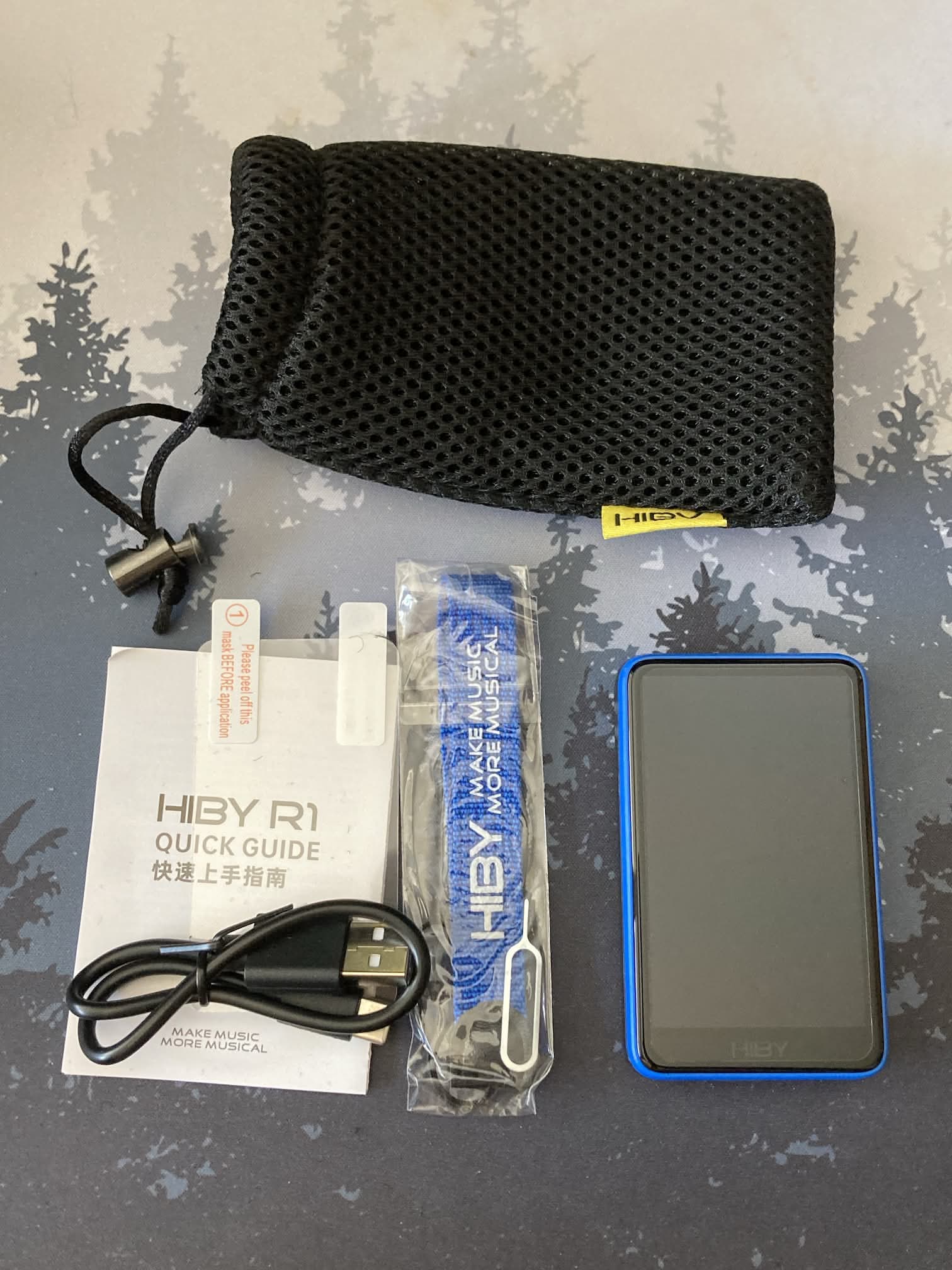 DAP Hiby R1 con accesorios: bolsa, cable USB-C, instrucciones, protector de pantalla y correa de tela.